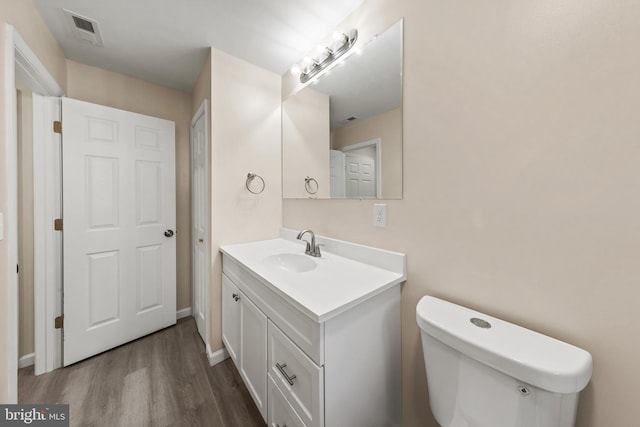 half bath featuring vanity, wood finished floors, visible vents, baseboards, and toilet