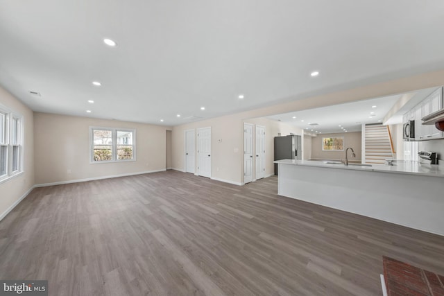 unfurnished living room featuring light wood-style flooring, recessed lighting, baseboards, and a sink