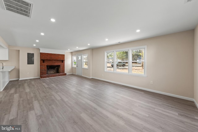 unfurnished living room with visible vents, a brick fireplace, electric panel, recessed lighting, and light wood-style floors