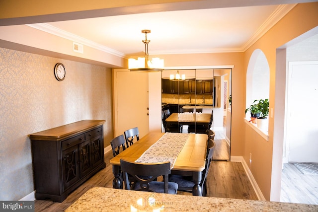 dining space with light wood-type flooring, crown molding, and a notable chandelier