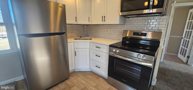 kitchen featuring appliances with stainless steel finishes, light wood-type flooring, white cabinets, decorative backsplash, and sink