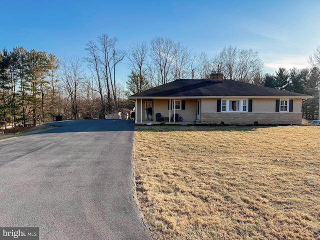 single story home featuring aphalt driveway, a chimney, covered porch, a front yard, and stone siding