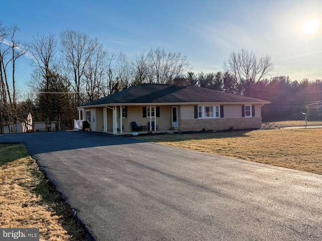 view of front of house with driveway, stone siding, a chimney, covered porch, and a front yard