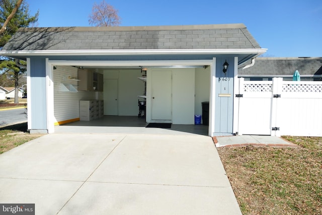 garage with a gate, concrete driveway, and fence