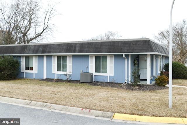 ranch-style home with mansard roof, roof with shingles, central AC, and a front lawn