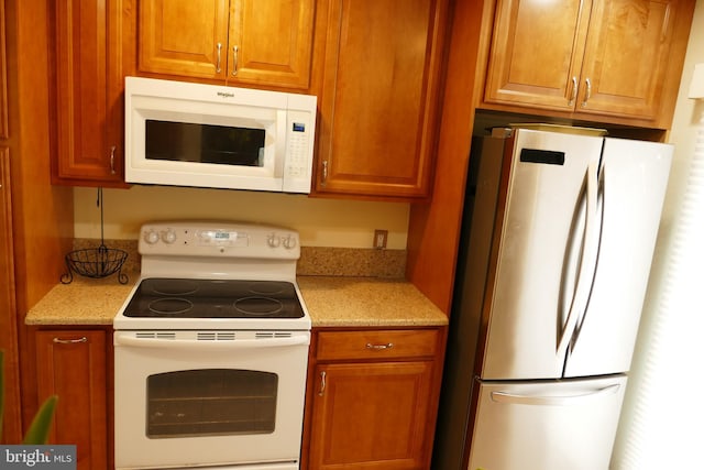 kitchen featuring brown cabinets, white appliances, and light stone countertops