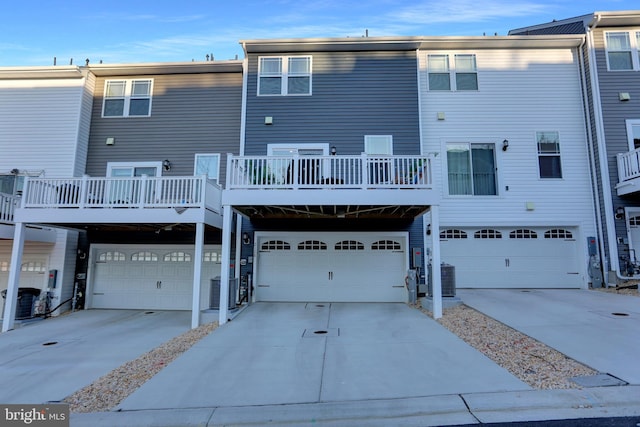 back of house featuring driveway, central AC unit, an attached garage, and a balcony