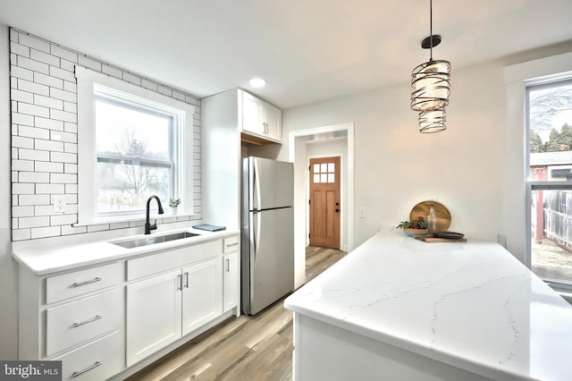 kitchen with white cabinetry, sink, decorative light fixtures, and stainless steel refrigerator