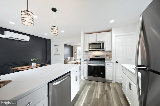 kitchen featuring a wall mounted AC, hanging light fixtures, stainless steel appliances, light hardwood / wood-style floors, and white cabinets