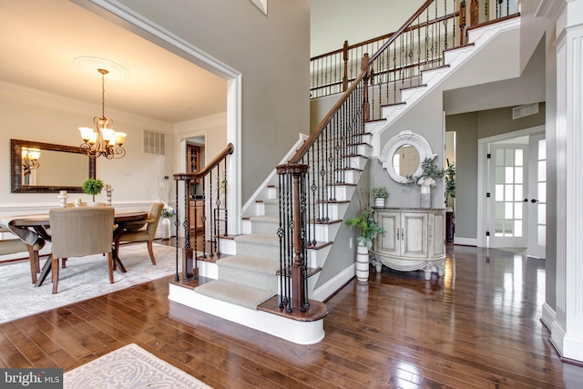 stairs featuring ornamental molding, a towering ceiling, an inviting chandelier, and wood-type flooring