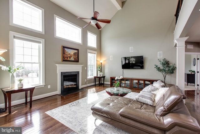 living room with decorative columns, a fireplace, a towering ceiling, ceiling fan, and dark hardwood / wood-style floors