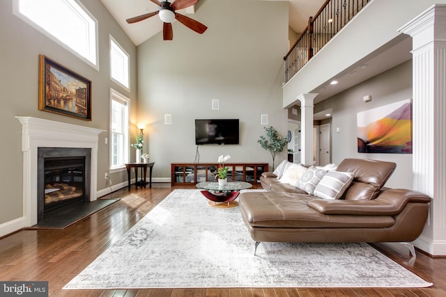 living room with ceiling fan, ornate columns, a high ceiling, and dark hardwood / wood-style flooring