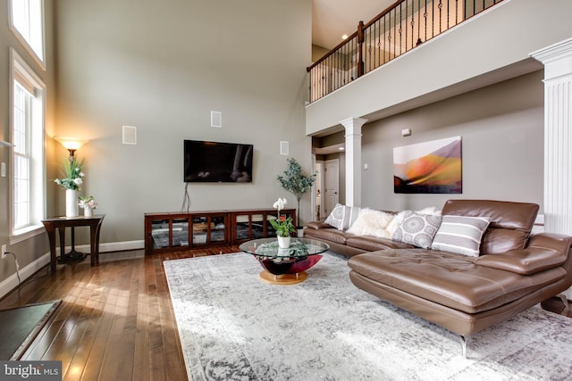 living room with decorative columns, a towering ceiling, and hardwood / wood-style floors