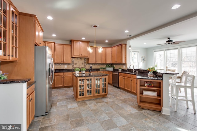 kitchen with appliances with stainless steel finishes, hanging light fixtures, a kitchen breakfast bar, an island with sink, and dark stone counters