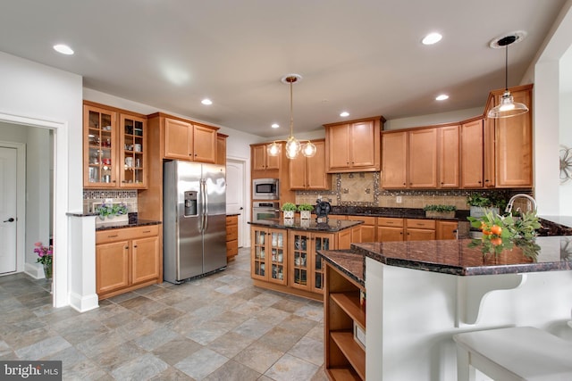 kitchen featuring decorative light fixtures, stainless steel appliances, a kitchen bar, and dark stone counters