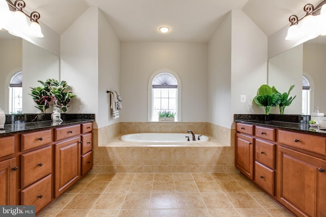 bathroom with tile patterned flooring, vanity, and a relaxing tiled tub