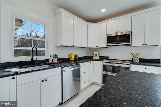 kitchen with dark stone countertops, recessed lighting, a sink, white cabinets, and appliances with stainless steel finishes