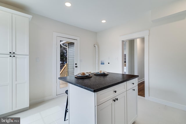 kitchen featuring a kitchen breakfast bar, dark countertops, a center island, white cabinetry, and recessed lighting