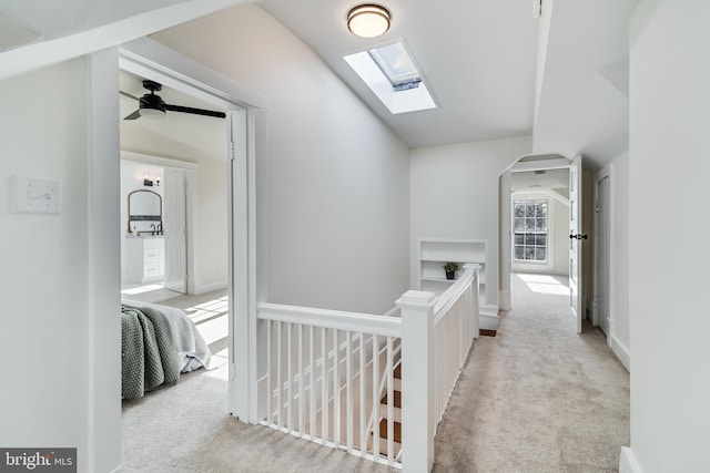 corridor featuring an upstairs landing, vaulted ceiling with skylight, baseboards, and carpet floors