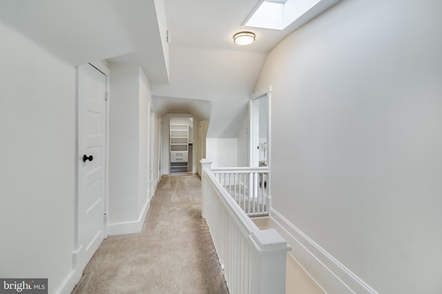 corridor with baseboards, an upstairs landing, vaulted ceiling with skylight, and carpet flooring