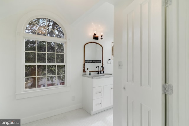 bathroom with vanity, lofted ceiling, a healthy amount of sunlight, and baseboards