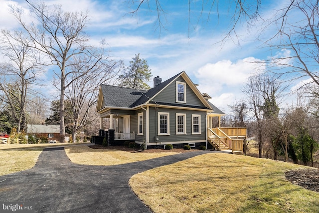 view of front of property with a front lawn, aphalt driveway, roof with shingles, covered porch, and a chimney