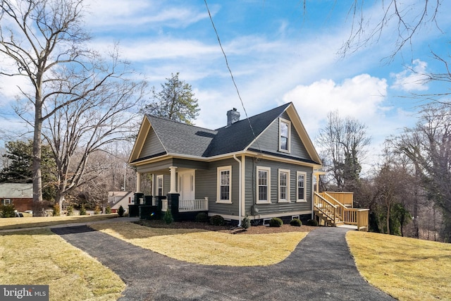 view of home's exterior featuring driveway, a yard, roof with shingles, covered porch, and a chimney