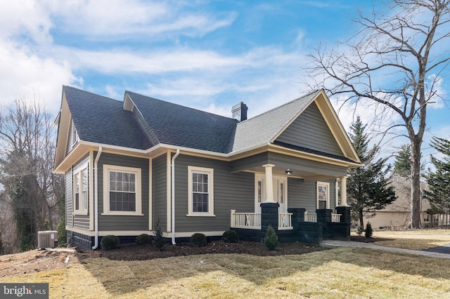 view of front of house featuring a front lawn, central AC, roof with shingles, covered porch, and a chimney