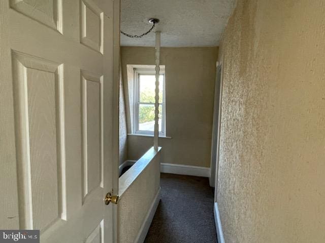 corridor featuring dark colored carpet and a textured ceiling