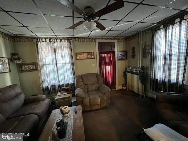 living room featuring a healthy amount of sunlight, radiator heating unit, a drop ceiling, and ceiling fan