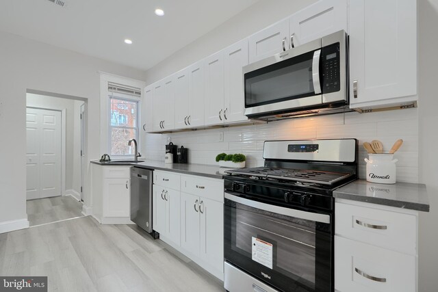 kitchen with tasteful backsplash, dark countertops, stainless steel appliances, white cabinetry, and a sink