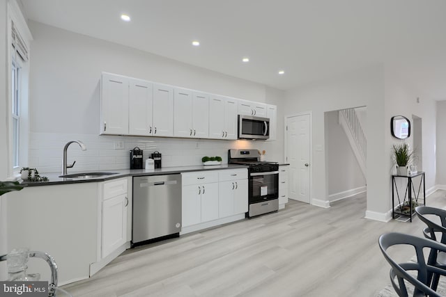 kitchen with dark countertops, decorative backsplash, appliances with stainless steel finishes, white cabinetry, and a sink