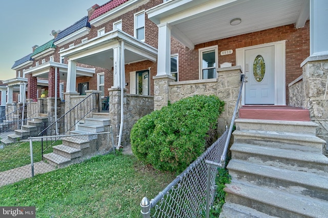 view of exterior entry featuring a tile roof, stone siding, brick siding, and fence