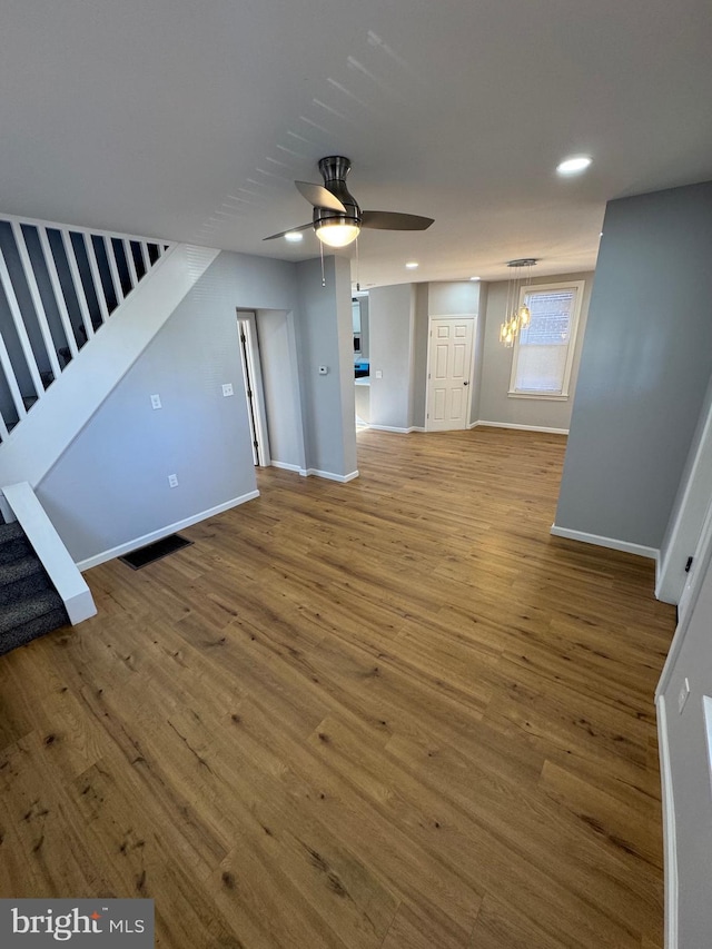 unfurnished living room with ceiling fan with notable chandelier and hardwood / wood-style floors