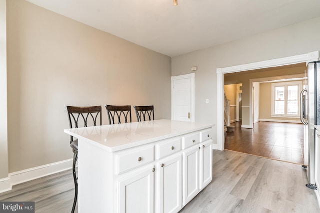 kitchen with a breakfast bar, a kitchen island, white cabinets, light stone countertops, and light wood finished floors