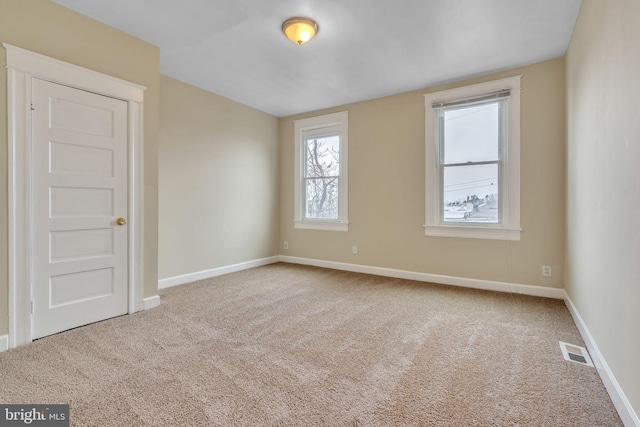 unfurnished room with carpet, visible vents, and baseboards