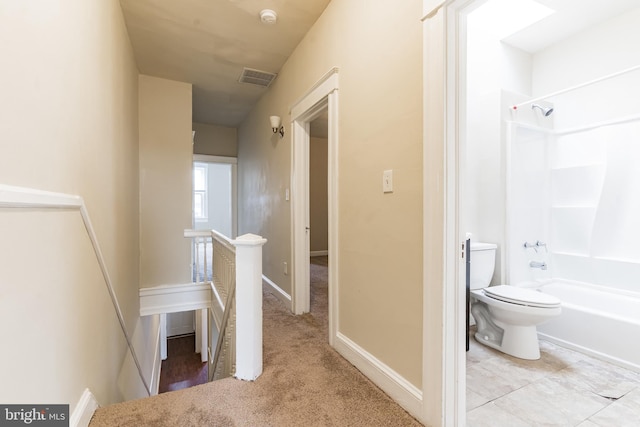 hall with baseboards, visible vents, and an upstairs landing