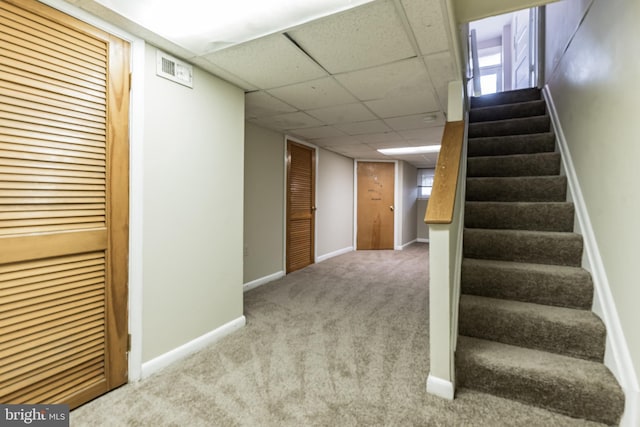 finished basement with stairs, baseboards, visible vents, and light colored carpet