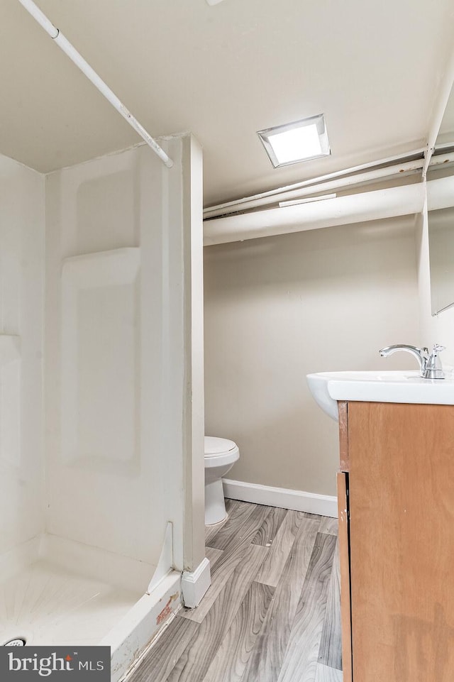 bathroom featuring toilet, a stall shower, vanity, wood finished floors, and baseboards