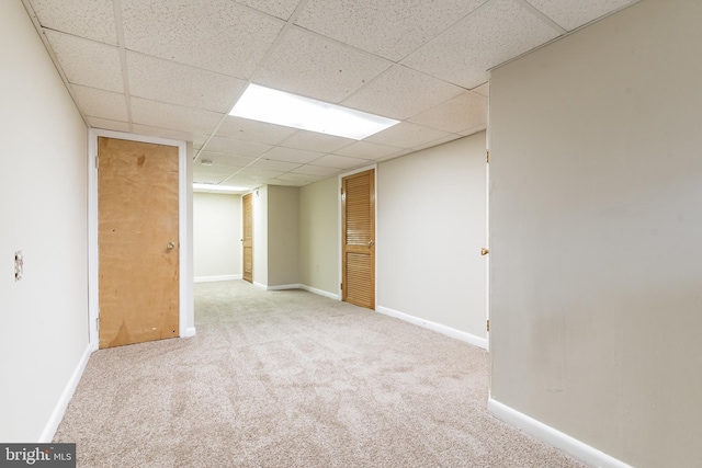 below grade area featuring light carpet, a drop ceiling, and baseboards