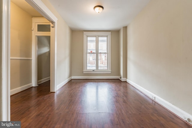 empty room with dark wood-style flooring and baseboards