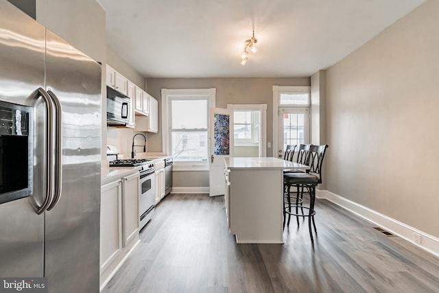 kitchen with a kitchen island, a kitchen breakfast bar, white cabinets, light countertops, and appliances with stainless steel finishes