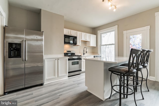 kitchen featuring light wood finished floors, stainless steel appliances, light countertops, white cabinetry, and a sink