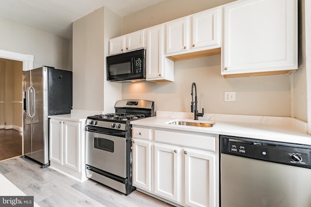 kitchen with light wood finished floors, stainless steel appliances, light countertops, white cabinetry, and a sink