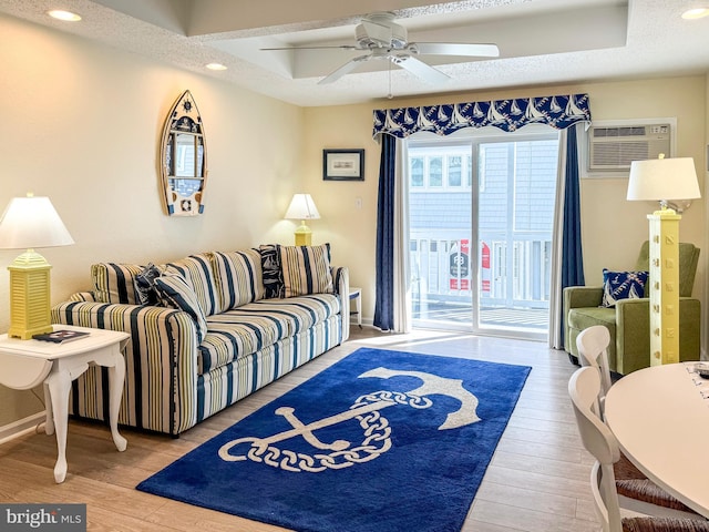 living room with a wall mounted air conditioner, hardwood / wood-style flooring, and a tray ceiling