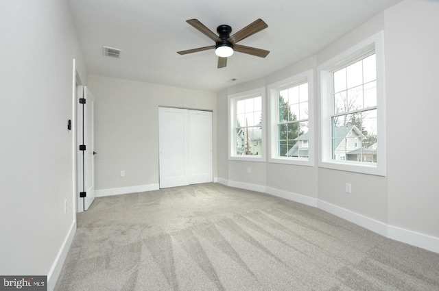 unfurnished bedroom with baseboards, multiple windows, visible vents, and light colored carpet