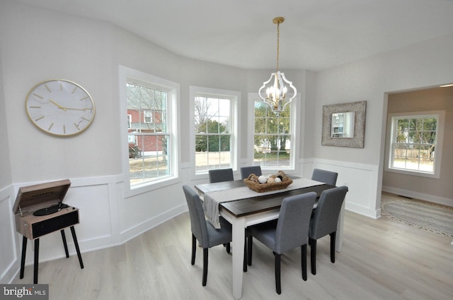 dining area with a decorative wall, wainscoting, light wood-style flooring, and an inviting chandelier