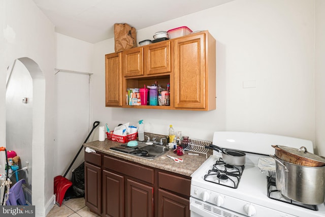 kitchen with arched walkways, light tile patterned floors, a sink, open shelves, and gas range gas stove