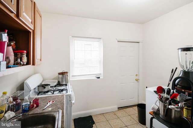 kitchen with brown cabinets, white gas stove, light tile patterned floors, a sink, and baseboards