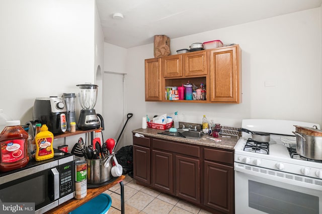 kitchen with light tile patterned floors, white gas stove, a sink, open shelves, and stainless steel microwave